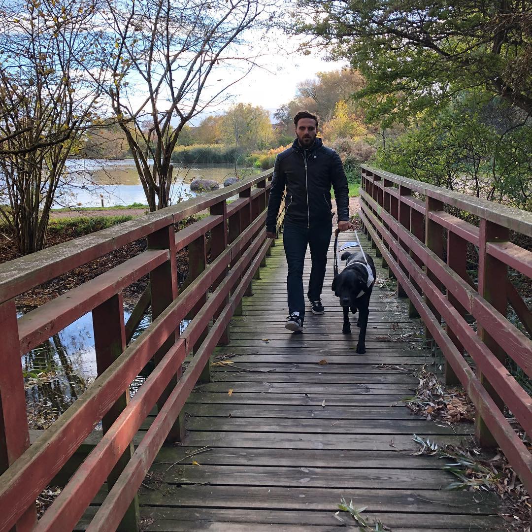 Bild på Fatmir som är ute och går med sin ledarhund på en träbro. En damm i bakgrunden