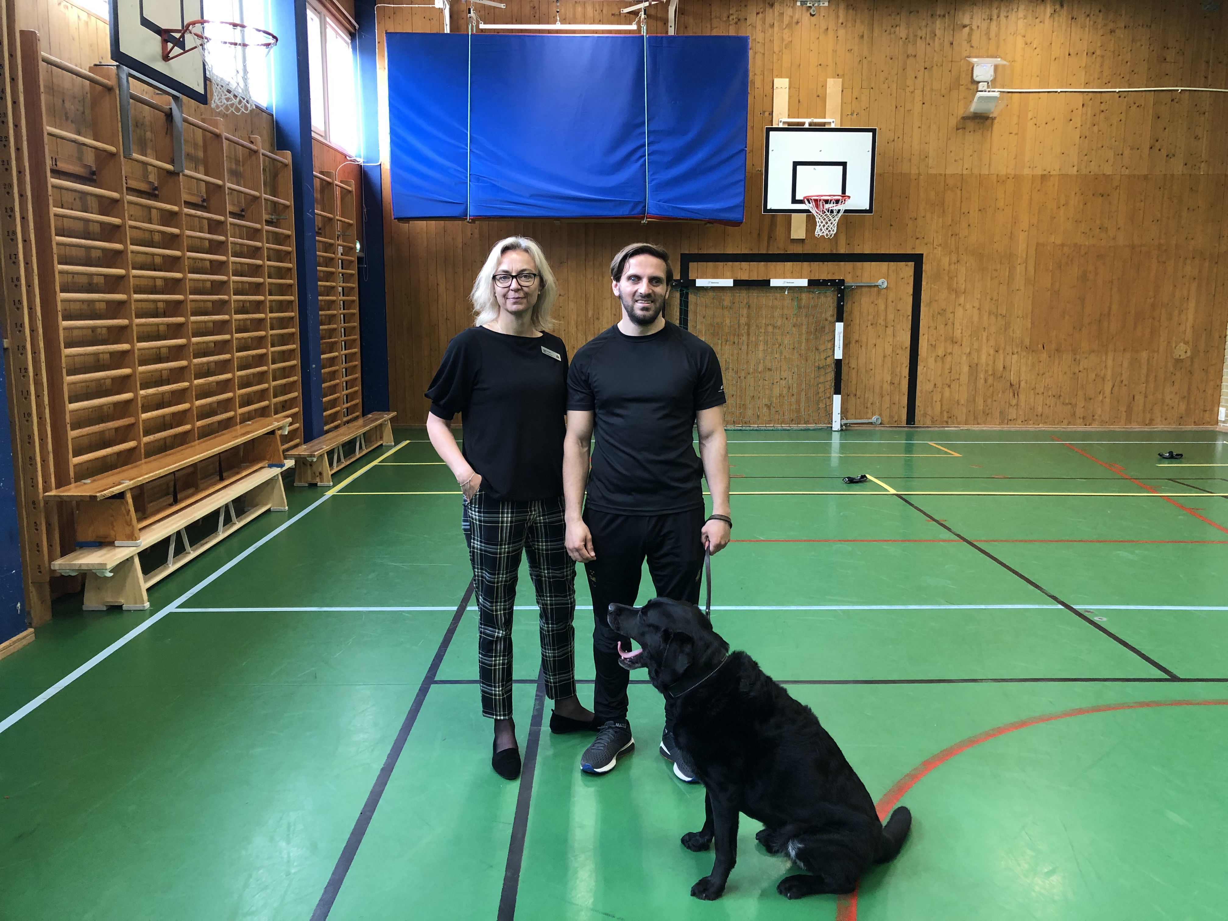 Fatmir står med rektor Ingela Svahn i idrottshallen på Värner Rydénskolan. Gibson står bredvid.